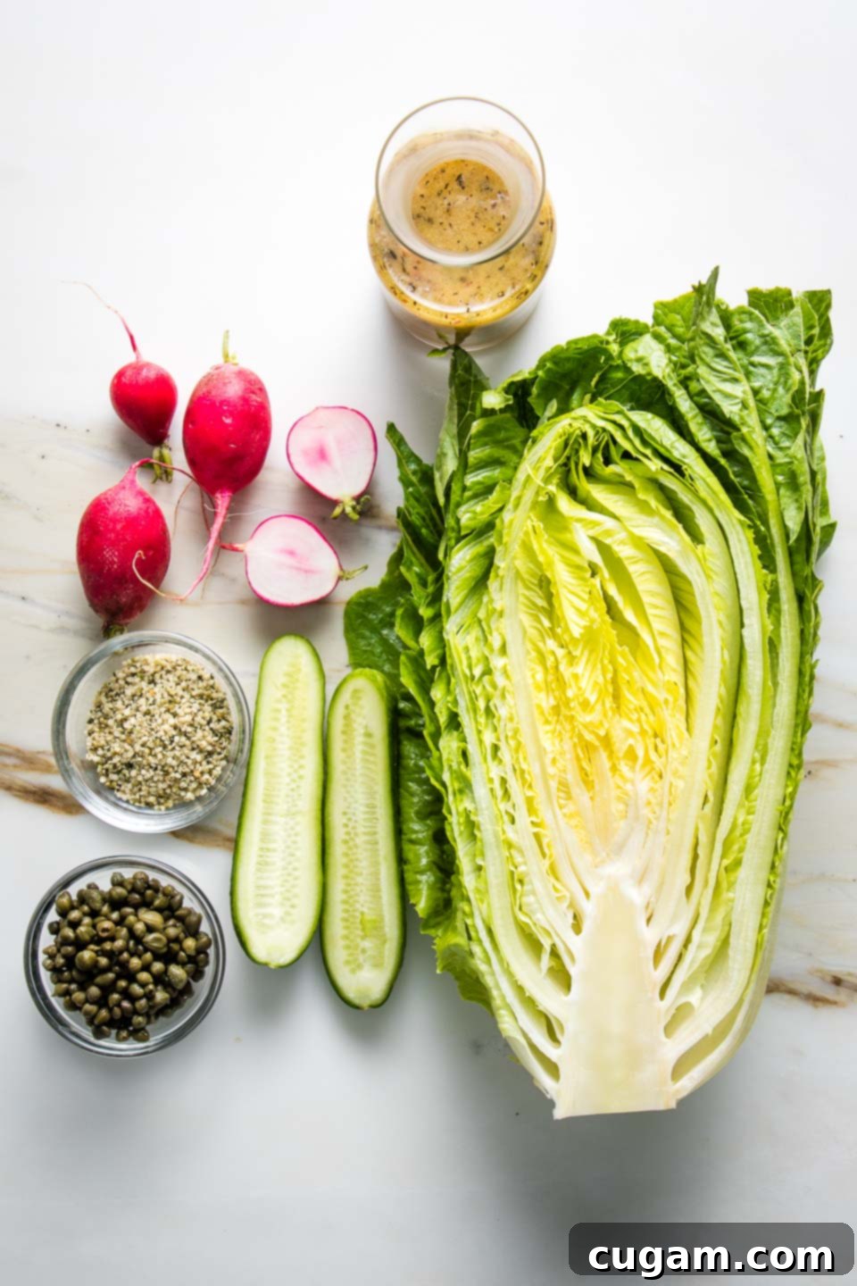 Fresh ingredients laid out for a vibrant green salad: a bowl of briny capers, crisp romaine lettuce, thinly sliced radishes, refreshing cucumbers, and a bottle of homemade salad dressing.