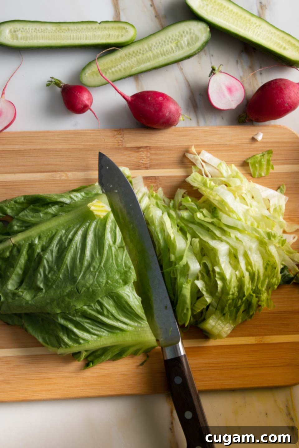 Demonstration of a chef precisely slicing romaine lettuce into thin, uniform strips using a sharp knife for an easy green salad.