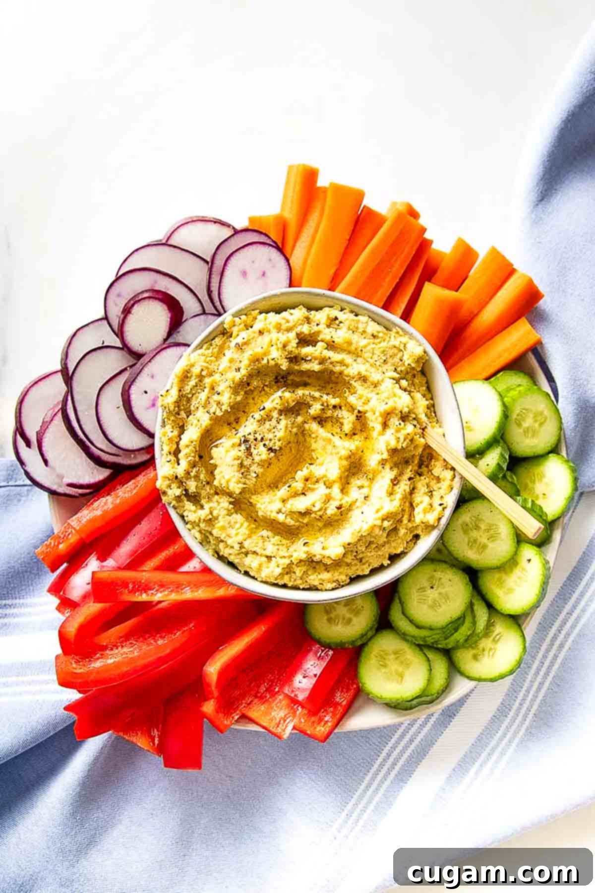 Hummus in a bowl, surrounded by vibrant sliced veggies. 