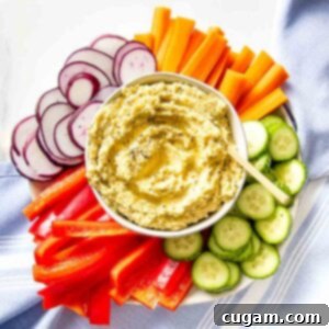 Bowl of hummus surrounded by colorful sliced veggies.