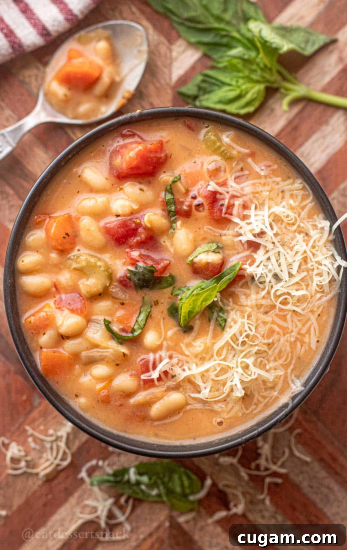 Bowl of cooked tuscan white bean soup on wooden cutting board with basil and shredded parmesan.