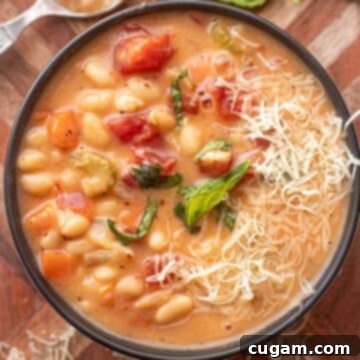 Bowl of cooked tuscan white bean soup on wooden cutting board with basil and shredded parmesan.