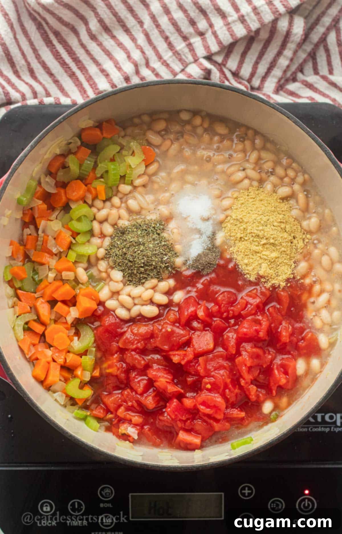 Tomatoes, beans, spices, and cooked carrots, celery, and onions in a pot.