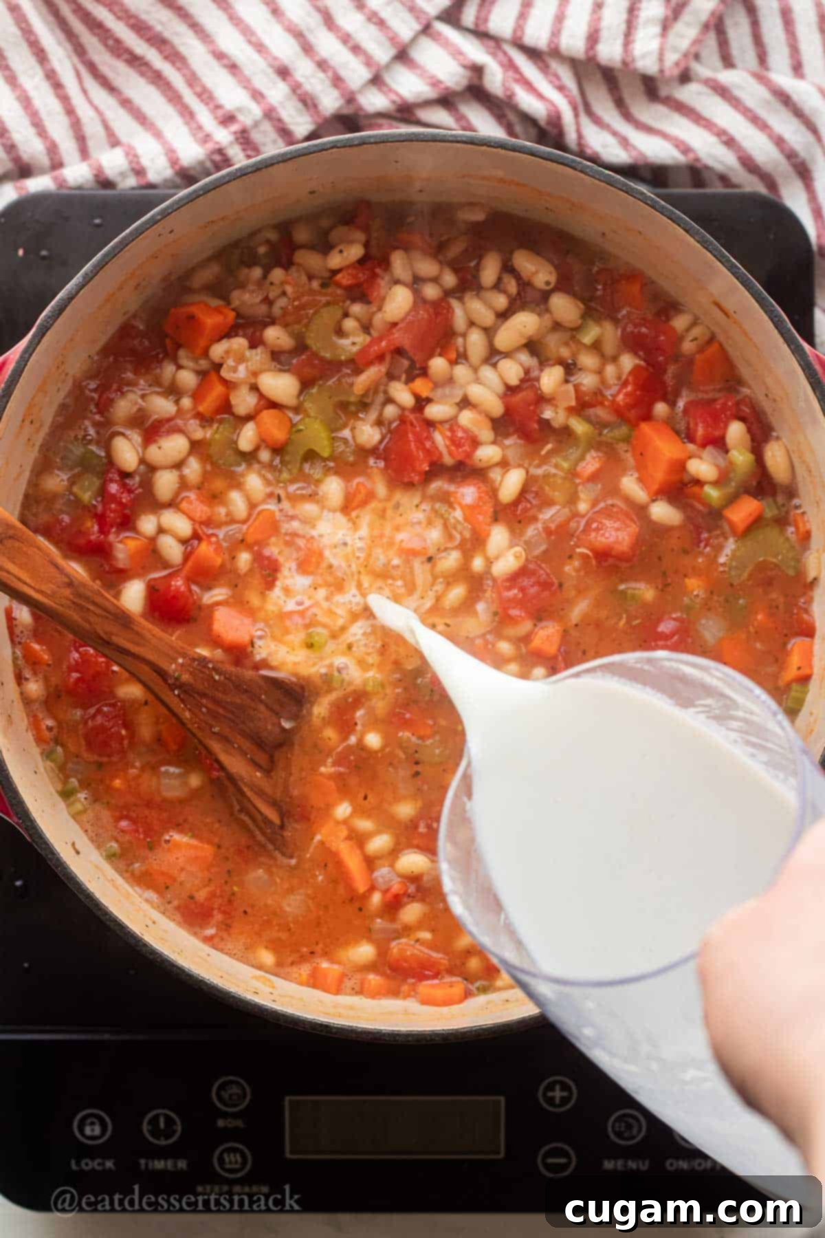 Pouring milk into pot of cooking italian white bean soup.