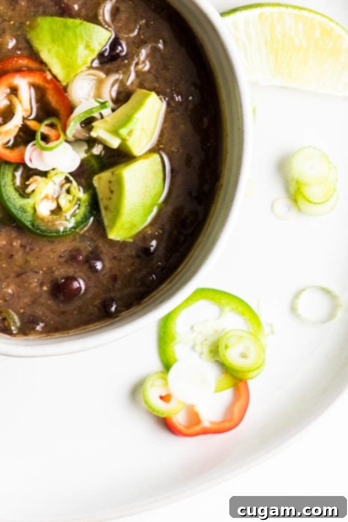 Simple Black Bean Bliss 11 A bowl of vegan black bean soup, beautifully garnished with creamy avocado chunks, spicy jalapeño slices, fresh lime wedges, and vibrant scallions, ready to be enjoyed.
