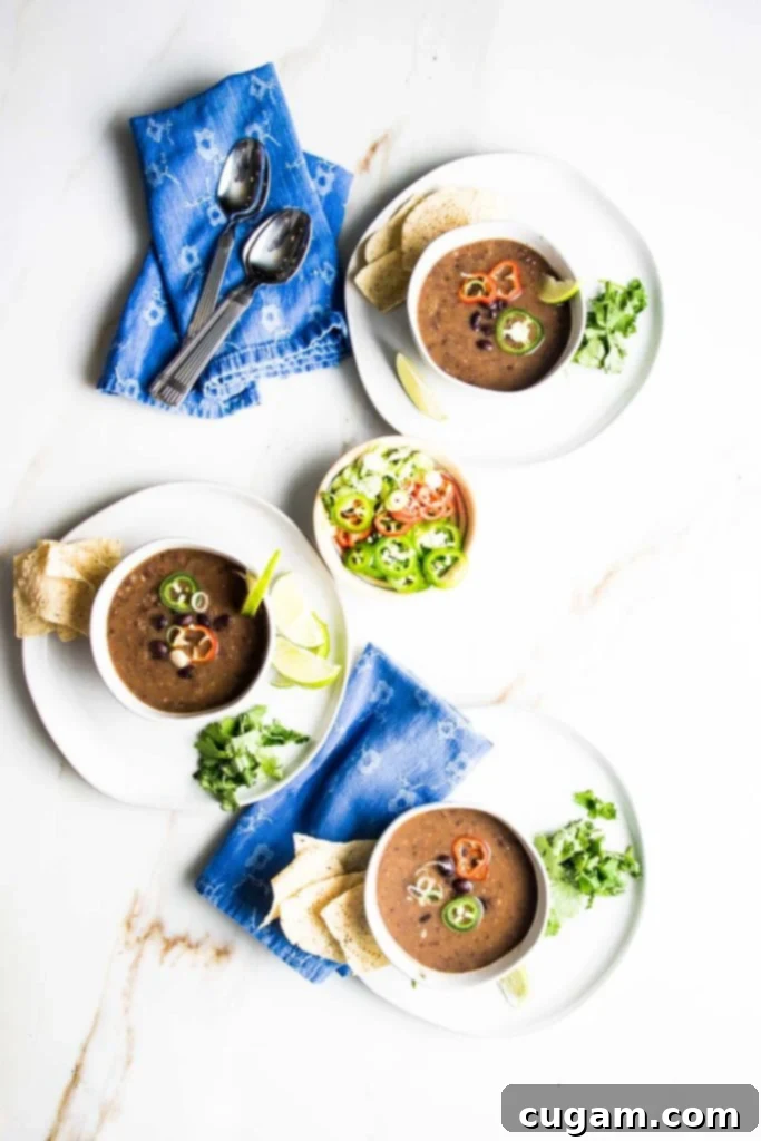 Multiple bowls of vegan black bean soup, each adorned with a variety of colorful and fresh toppings like avocado, cilantro, and vegan sour cream.