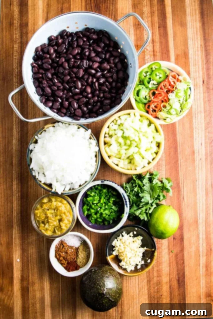 A colorful arrangement of fresh ingredients for vegan black bean soup, including black beans, chopped onions, celery, garlic, jalapeños, green chiles, cilantro, and spices.