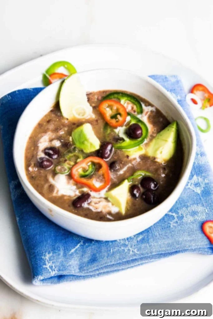 Close-up of a bowl of rich black bean soup topped with creamy avocado slices, spicy jalapeños, and fresh green scallions.
