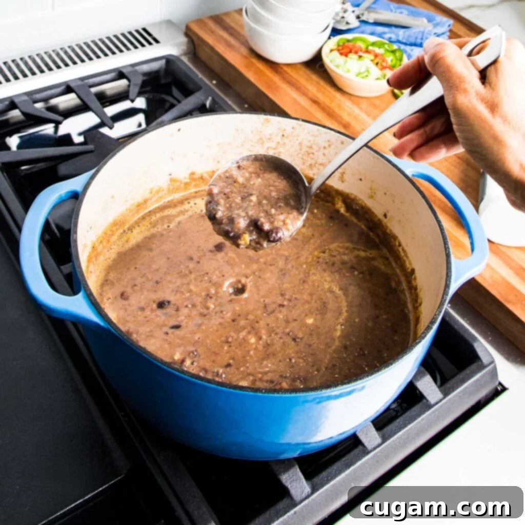A ladle scooping hearty vegan black bean soup from a blue Dutch oven, showcasing its rich, pureed texture with some whole beans.