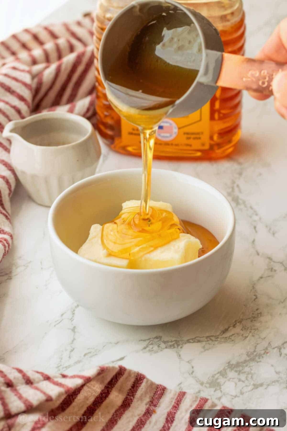 Pouring honey into white bowl of softened butter.