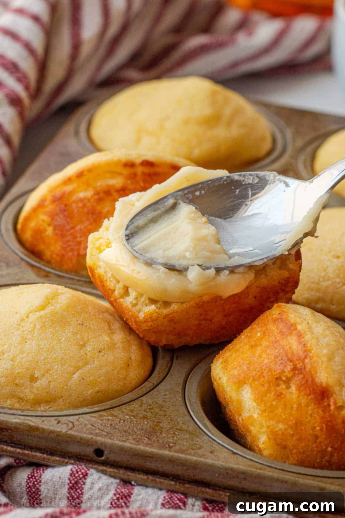 Baked cornbread muffin with honey butter spreading on with a spoon.