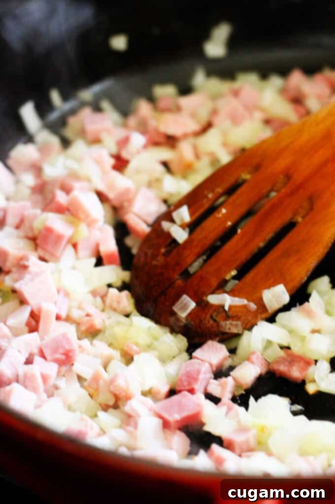 Diced ham and chopped onions sautéing in a pan, releasing their aromatic flavors.