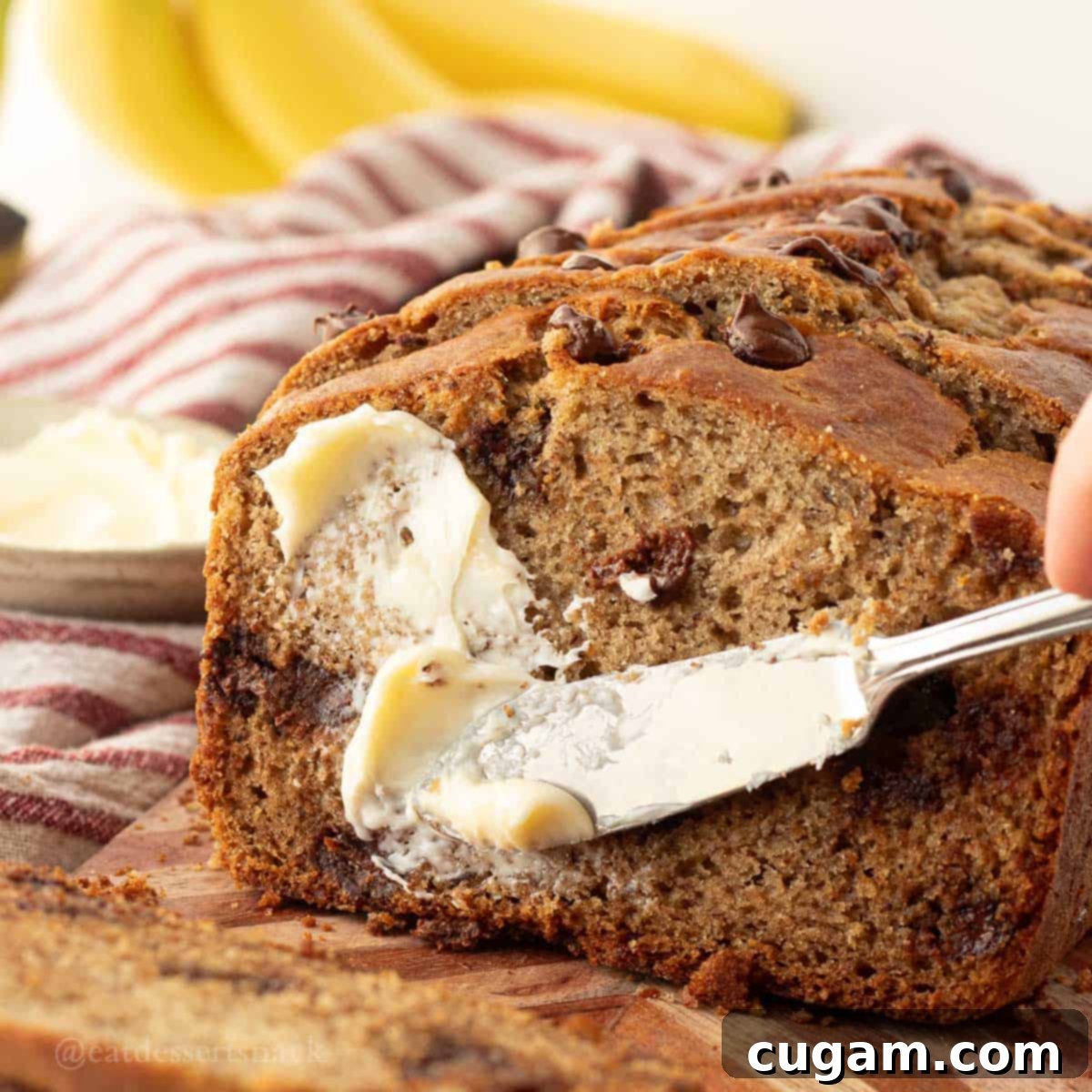 Elevated Sourdough Banana Bread 11 A knife spreading honey butter over a thick slice of freshly baked sourdough discard banana bread.