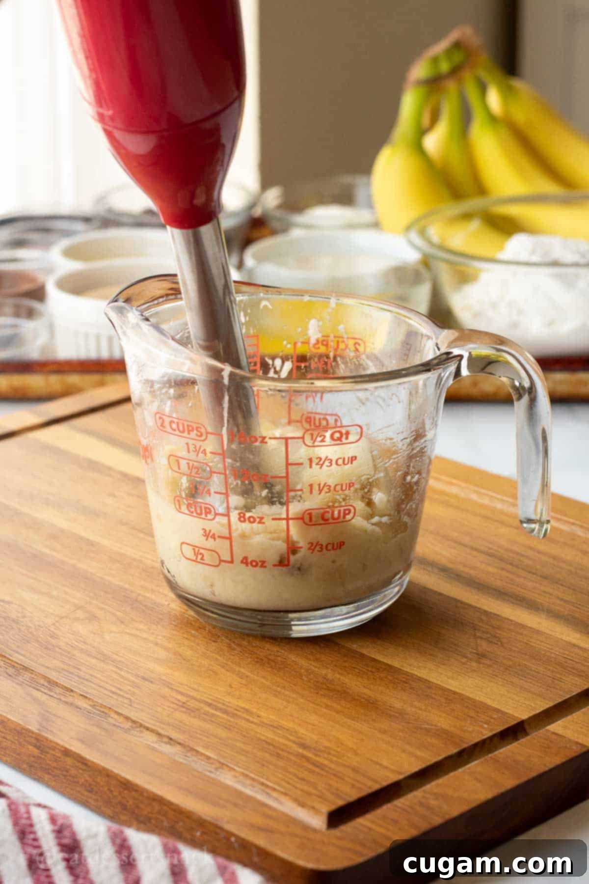Elevated Sourdough Banana Bread 4 Mashing ripe bananas in a glass measuring cup with an immersion blender.
