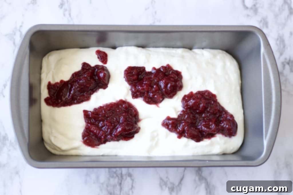 No Churn Cherry Cheesecake Ice cream with graham cracker crumbles, vanilla, sweetened condensed milk, cream cheese, and cherry pie filling. Made with real cream because nothing else will do. Best summer dessert ever! #icecream #nochurnicecream #easydessert #cherrycheesecake #cherrydesserts #cheesecakedessert #fruitfilleddessert #summertreats A pan filled with whipped cream, with spoonfuls of vibrant cherry pie filling dotted on top, ready for swirling.