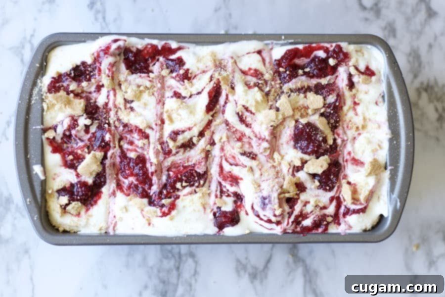 No Churn Cherry Cheesecake Ice cream with graham cracker crumbles, vanilla, sweetened condensed milk, cream cheese, and cherry pie filling. Made with real cream because nothing else will do. Best summer dessert ever! #icecream #nochurnicecream #easydessert #cherrycheesecake #cherrydesserts #cheesecakedessert #fruitfilleddessert #summertreats Crushed graham crackers generously sprinkled over the swirled whipped cream and cherry pie filling in a pan, adding a classic cheesecake texture.
