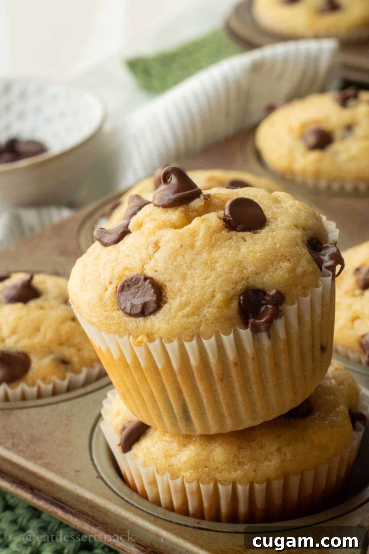 Tilted banana muffin on top of another mufifn in a muffin tin, showcasing its golden-brown top and fluffy texture.
