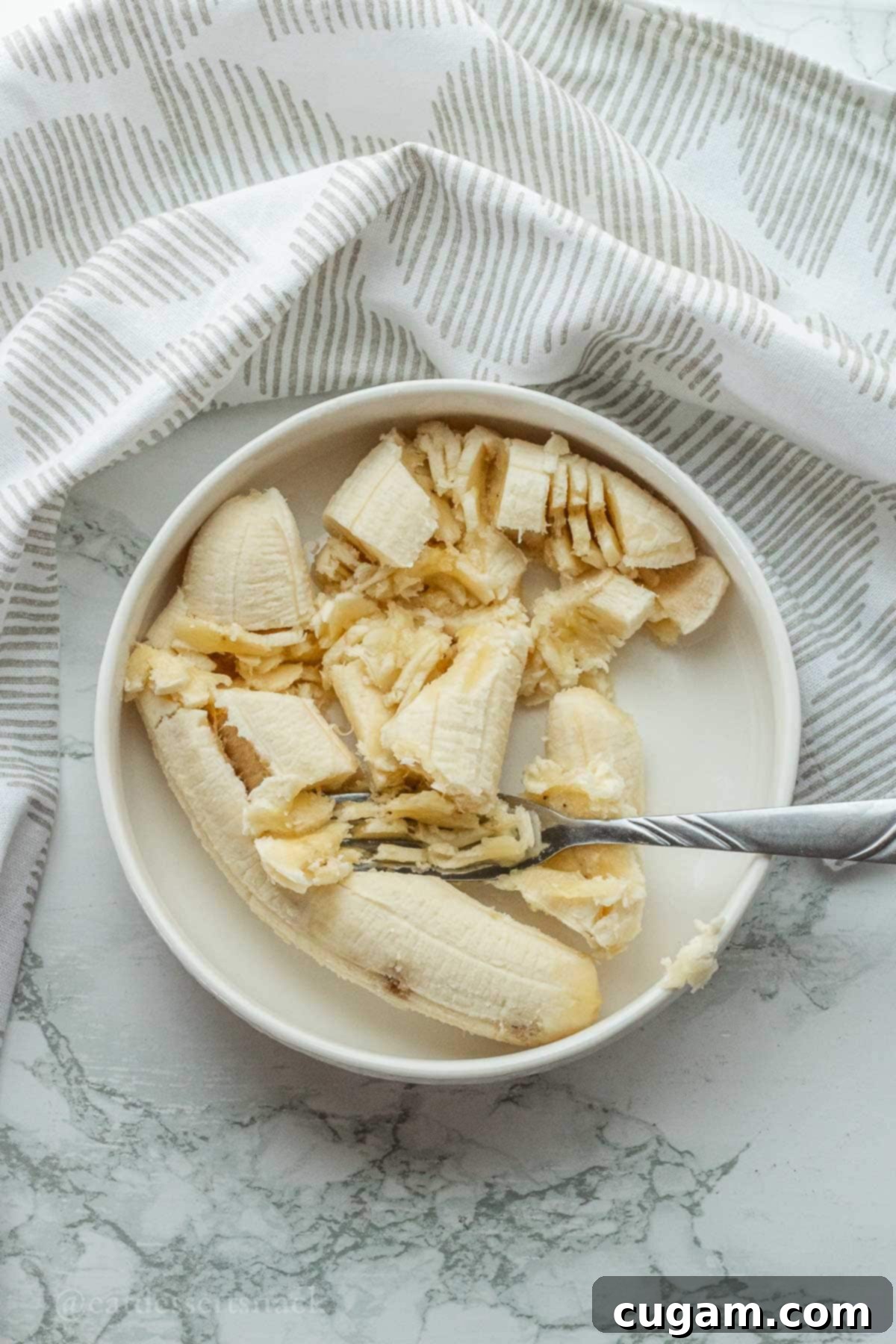Fork mashing banana on white plate.