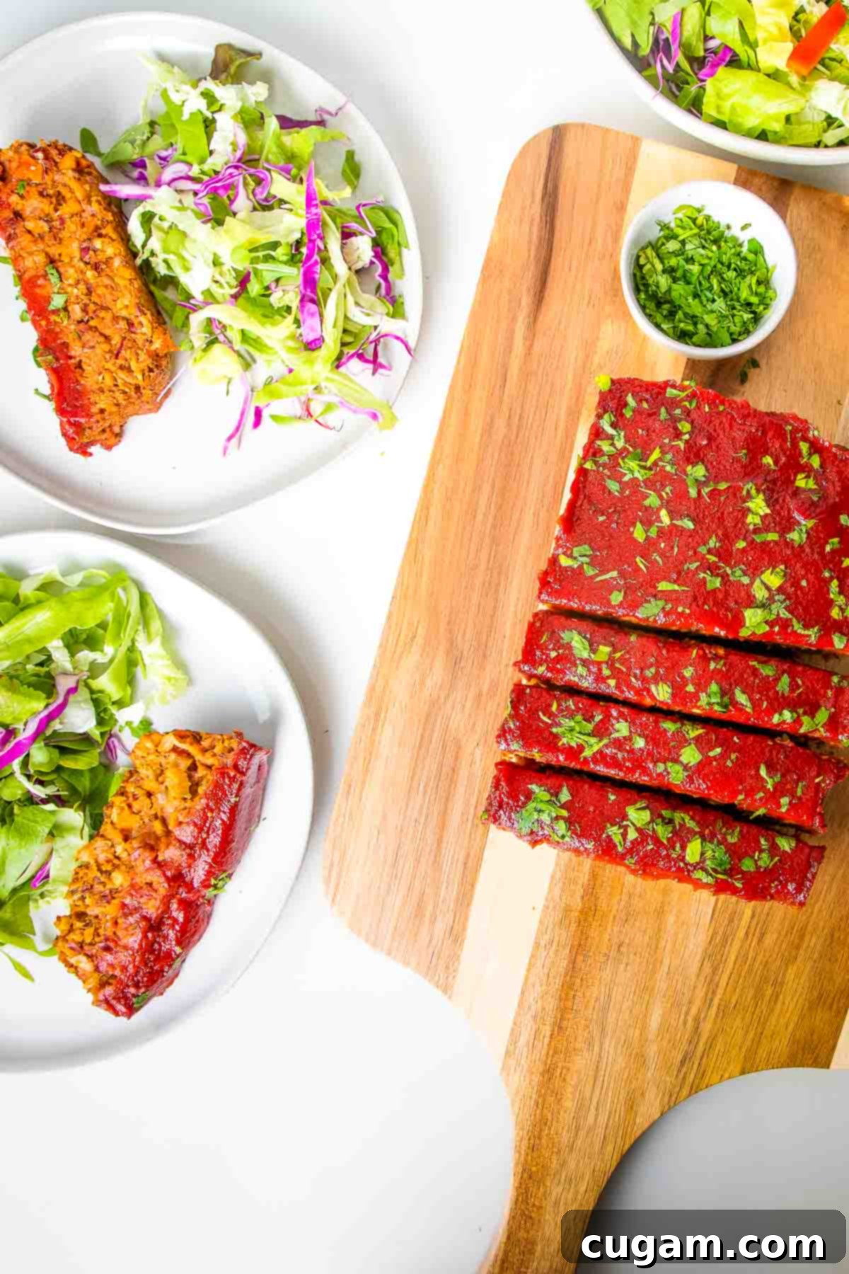 Sliced vegan meatloaf on a cutting board, with plates of meatloaf and a fresh side salad.