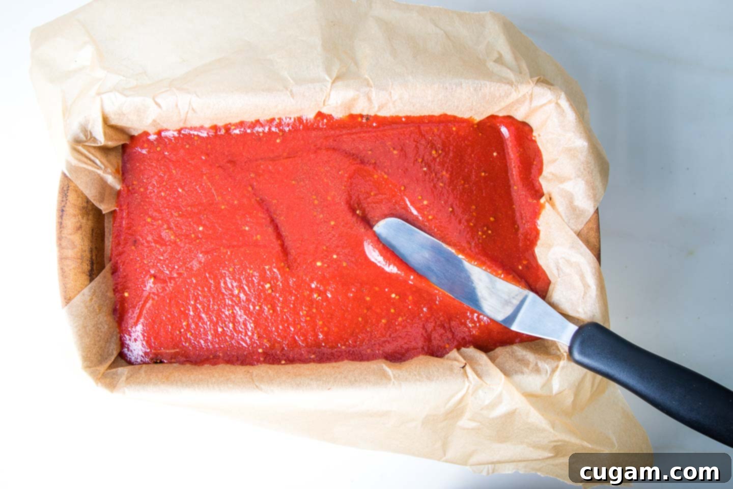 An offset spatula expertly spreading a luscious tomato mixture onto the top surface of the partially baked vegan meatloaf.