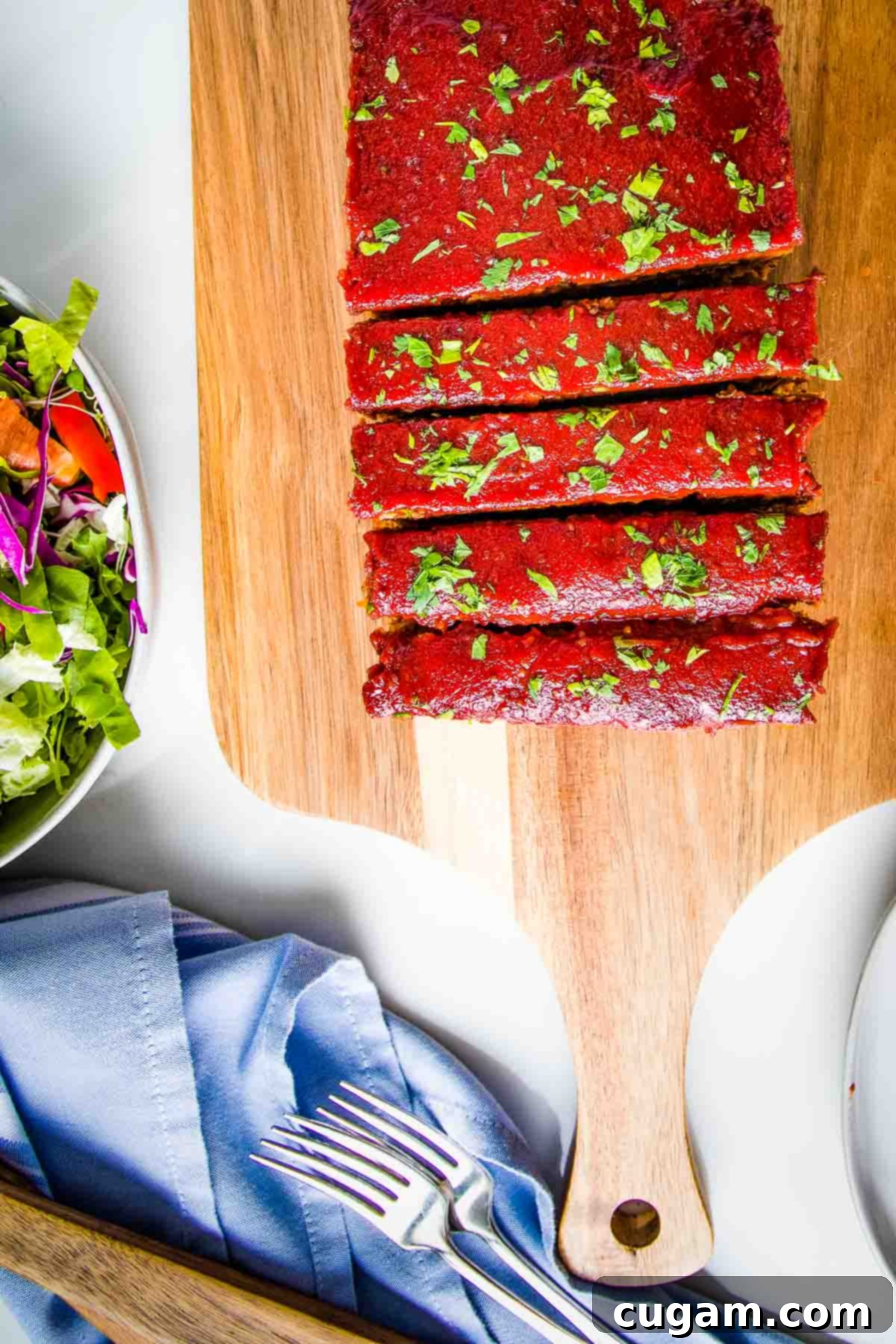 A beautifully presented vegan meatloaf, topped with a glistening tomato sauce glaze and fresh herbs, meticulously cut into thick, inviting slices.