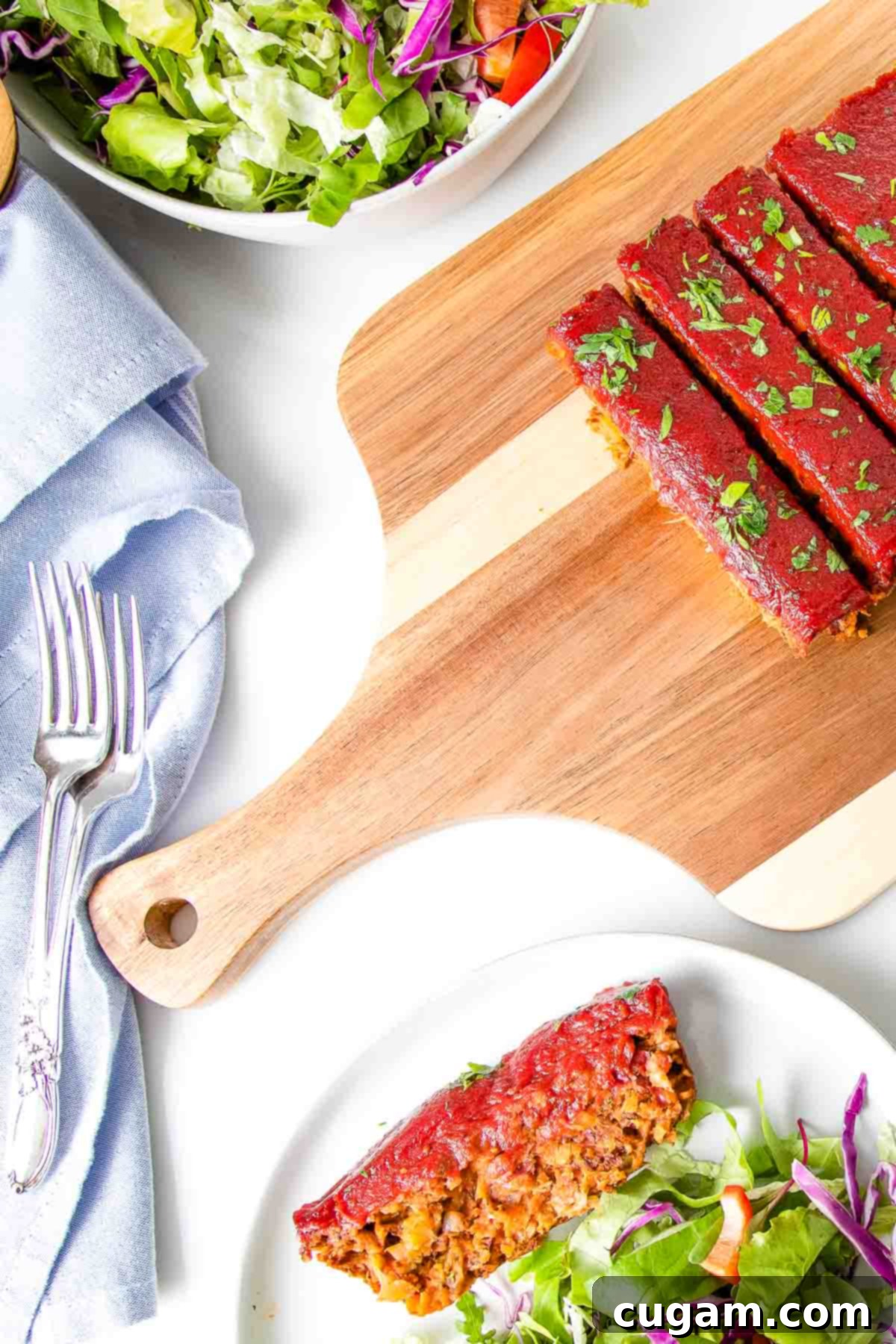 Beautifully sliced vegan meatloaf with a vibrant tomato glaze on a cutting board, accompanied by a plate with a slice of meatloaf and a fresh side salad, ready to be enjoyed.