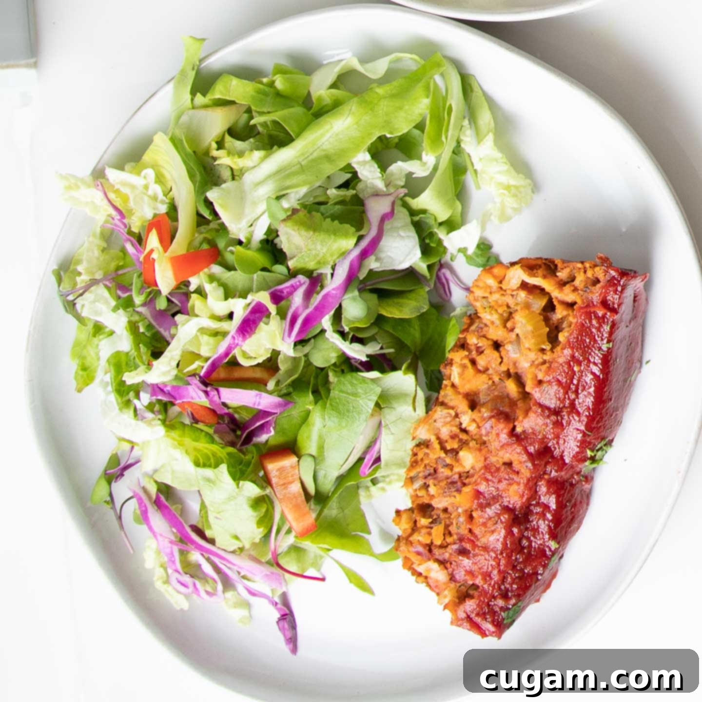 A delicious slice of vegan meatloaf paired with a simple, refreshing green salad on a white plate, ready for a healthy meal.