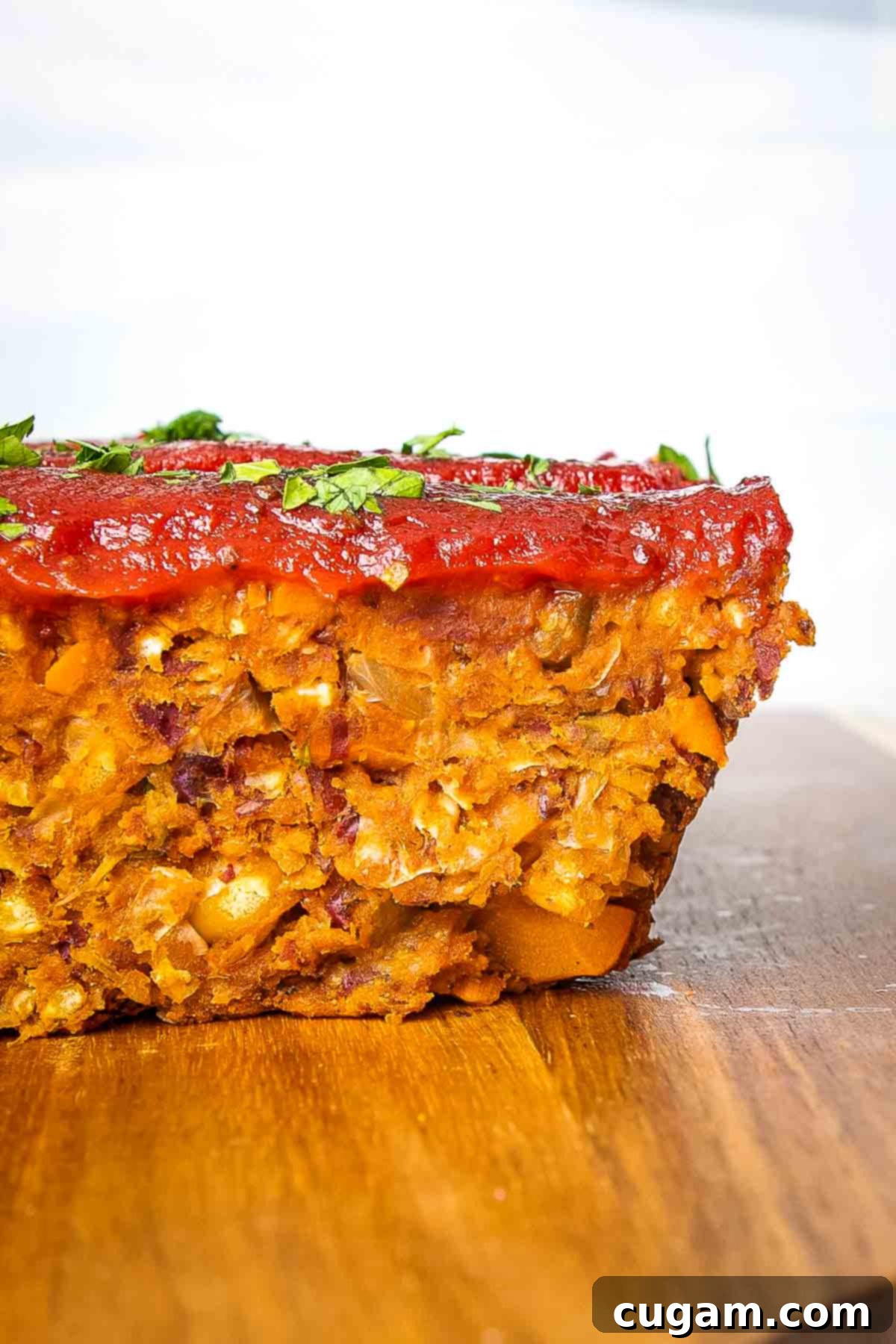 A side view of a perfectly sliced piece of vegan meatloaf, showcasing its rich texture and a luscious tomato glaze on top.