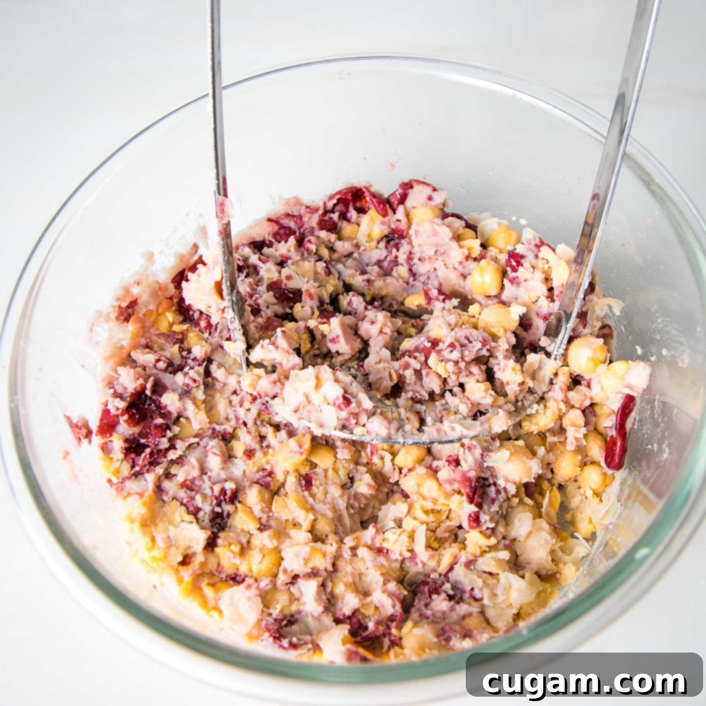 Mashing beans with a potato masher in a large glass mixing bowl, creating a coarse texture.