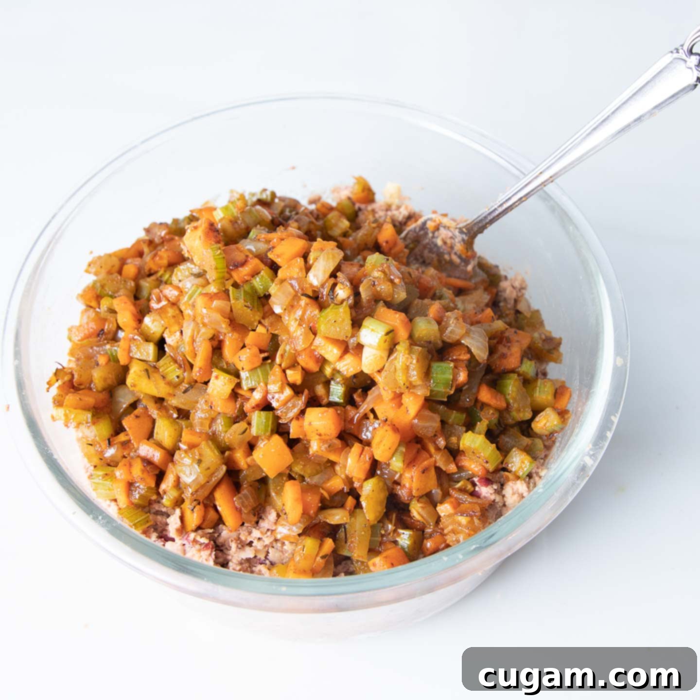 A large glass bowl holding a mixture of mashed beans and freshly sautéed vegetables, ready for final combination.