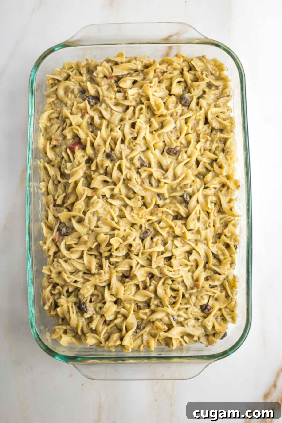 The unbaked apple noodle kugel, smoothly spread into a rectangular baking dish, ready to be placed in the oven and transformed into a golden, comforting dessert or side.