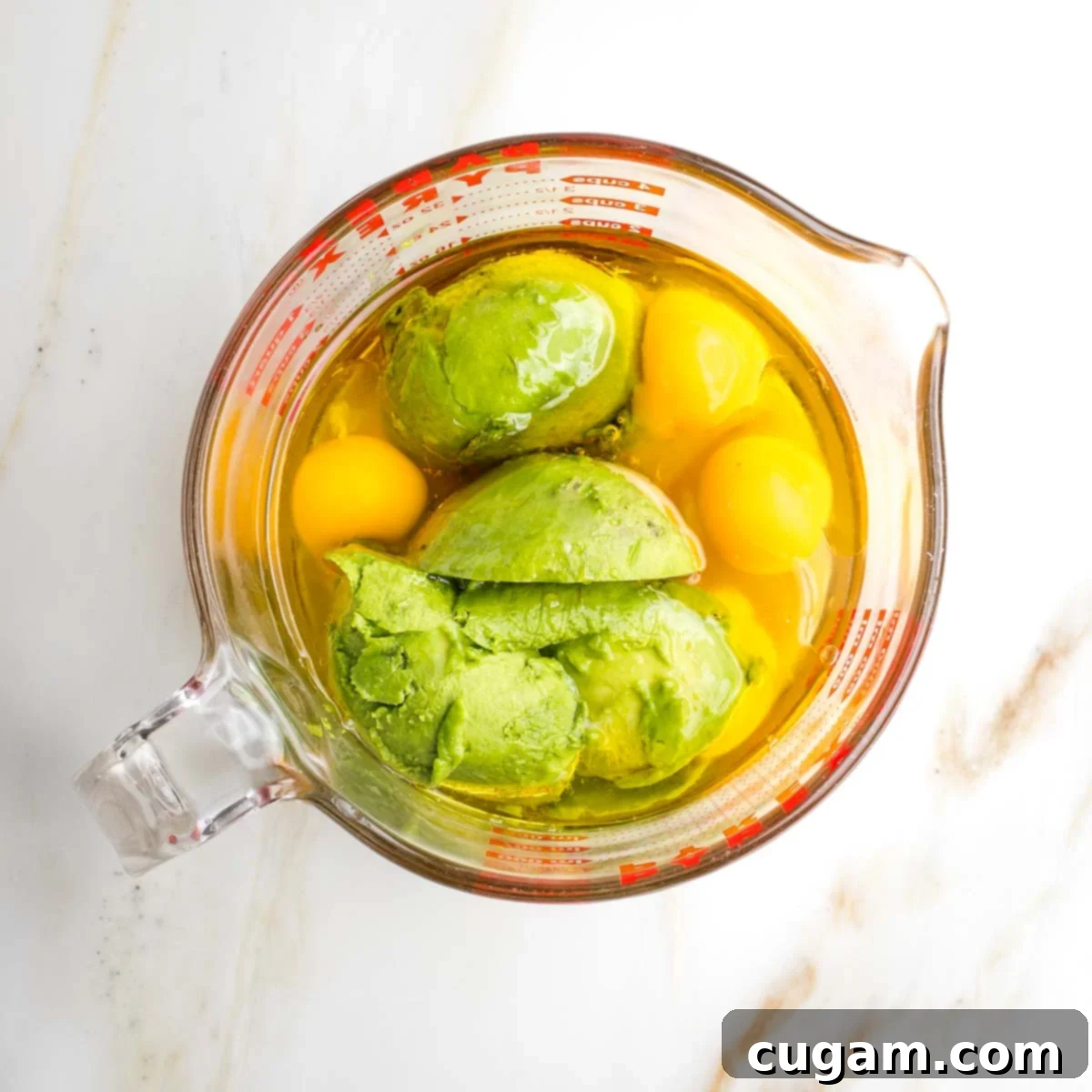 A close-up shot of whole eggs, creamy avocado, golden olive oil, and sweet honey, all gathered in a large measuring cup, ready to be blended into the kugel's rich, dairy-free base.