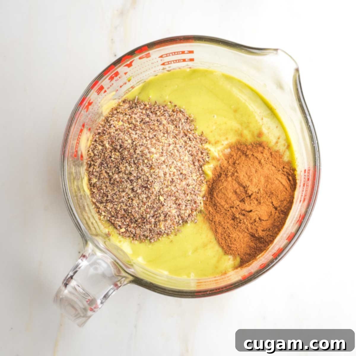 The light green, creamy avocado mixture now enhanced with the warm hues of ground flaxseed and aromatic cinnamon, ready for a final stir before blending with the main ingredients.