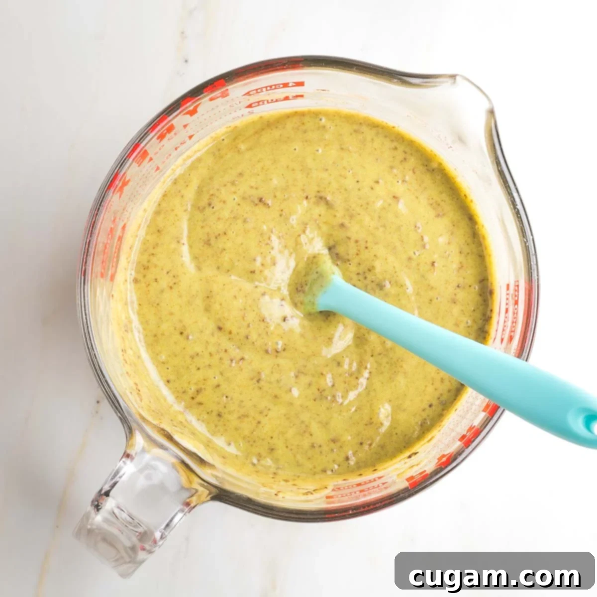 A textured, brownish-green mixture, now fully combined with ground flaxseed and cinnamon, swirling within a large measuring cup, showing a slightly grainy but unified consistency.