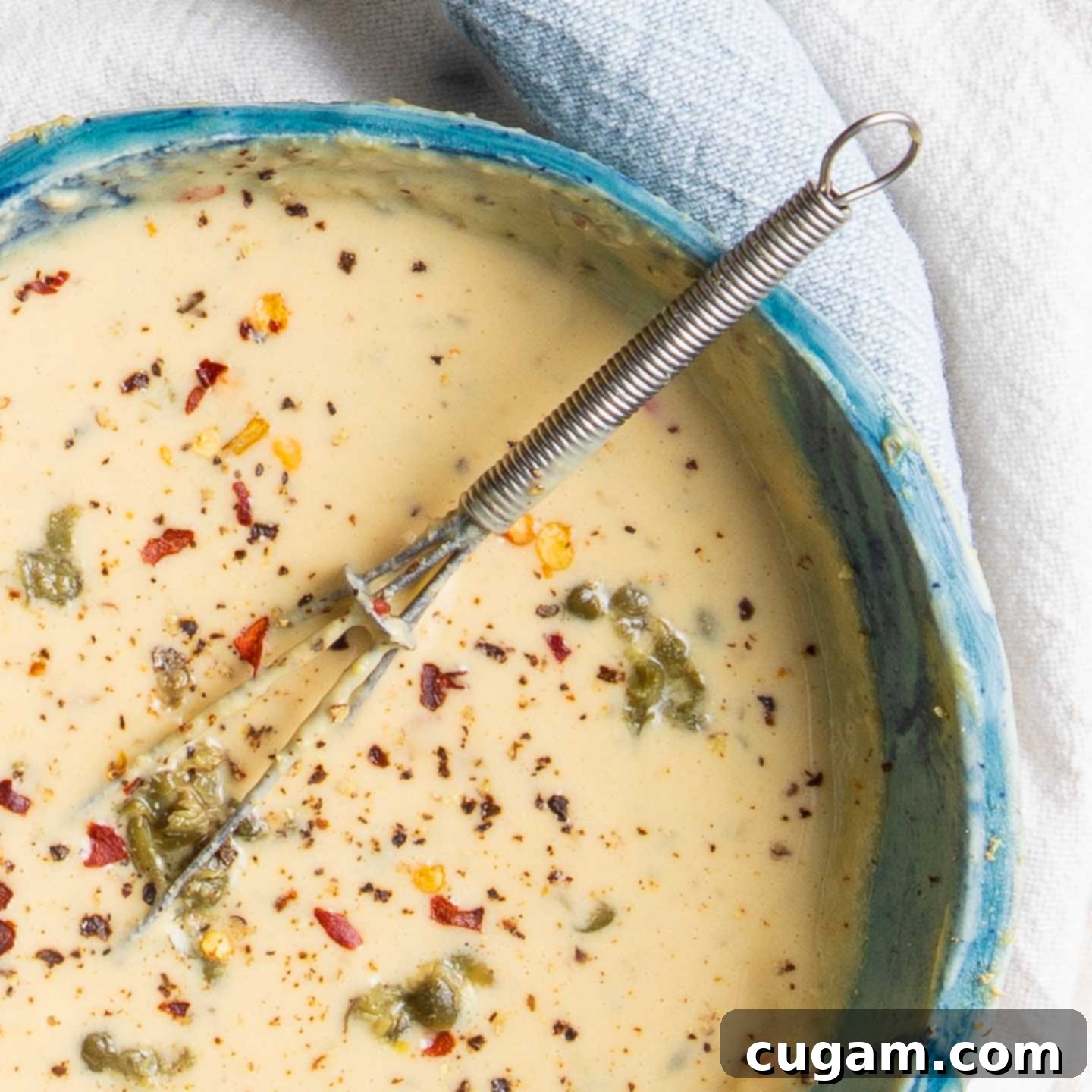 A close-up view of the smooth, creamy vegan tahini Caesar dressing in a glass bowl, visibly flecked with finely blended capers and a sprinkle of crushed red pepper, highlighting its rich texture and inviting appearance.