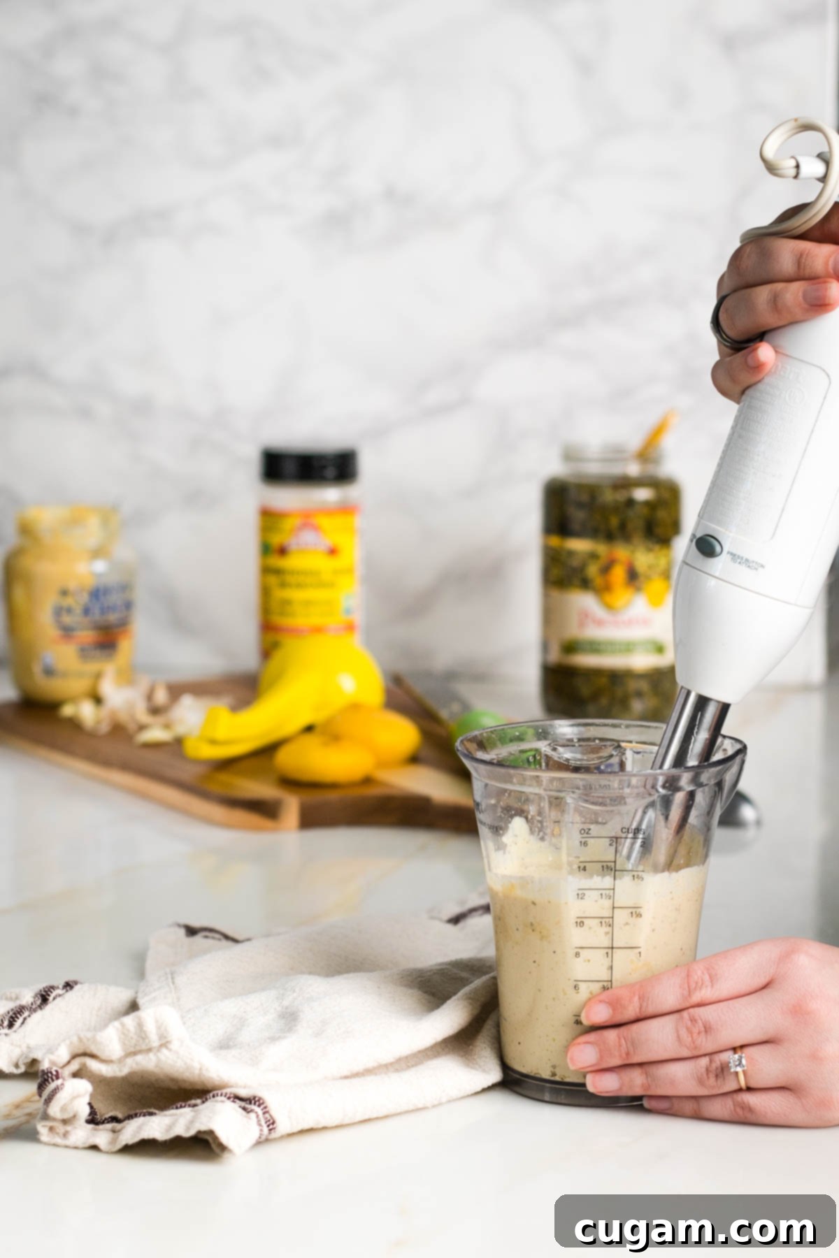 An immersion blender actively blending a creamy vegan Caesar dressing in a tall glass jar, showcasing the smooth, emulsified texture being created.