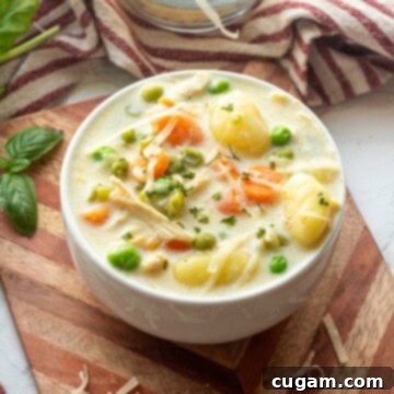 White bowl of chicken gnocchi soup on wood cutting board.