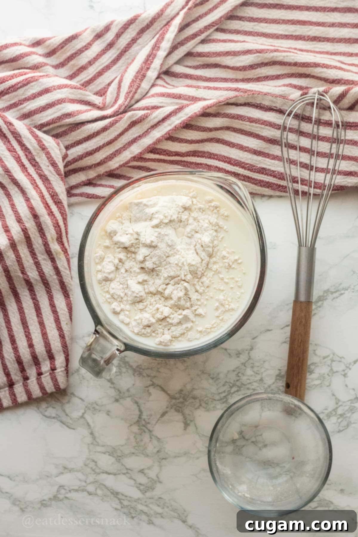 Milk and flour in measuring cup with wire whisk.