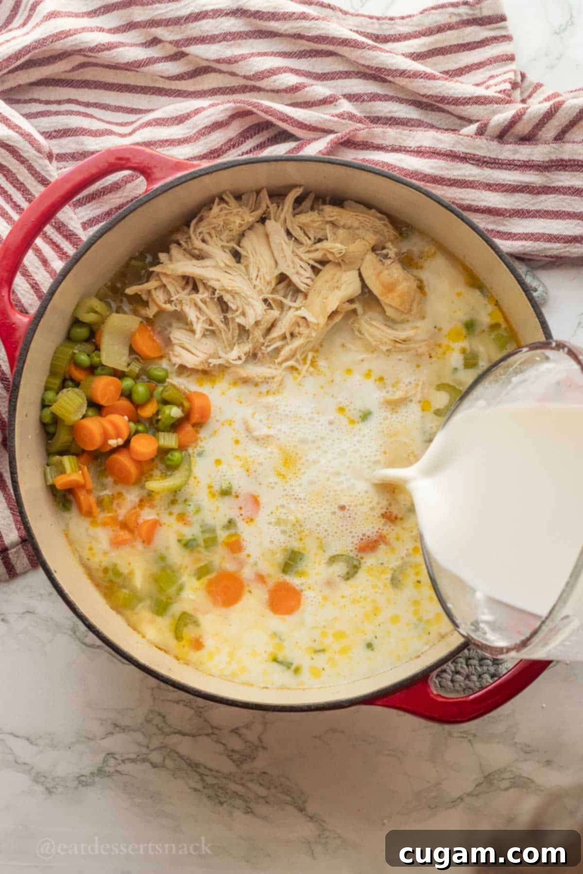 Pouring milk into pot with cooked vegetables and chicken.