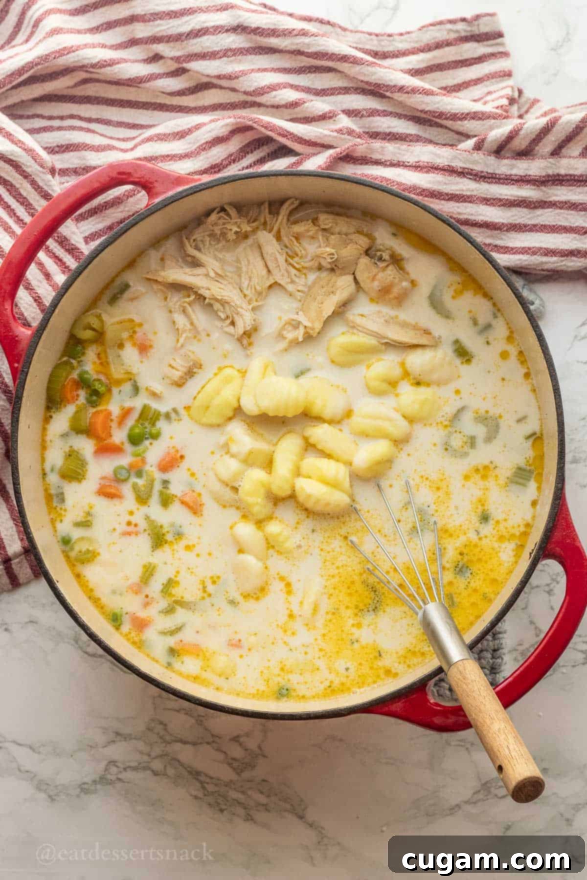 Raw gnocchi in pot with milk, chicken and vegetables with whisk.