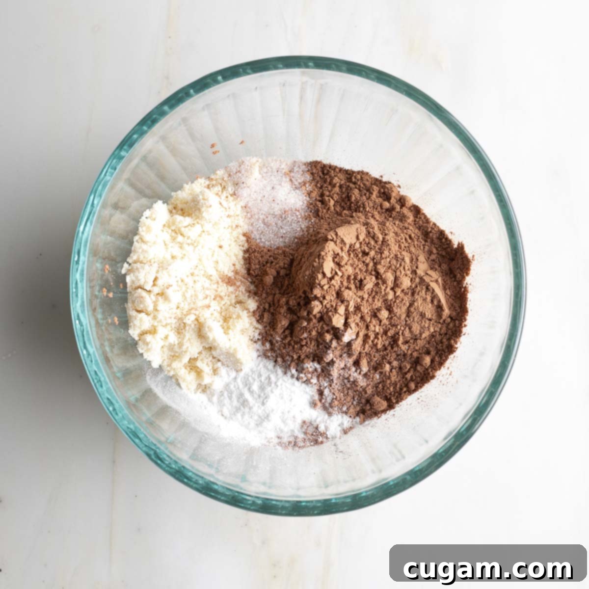 Dry ingredients for brownies, including cacao powder, almond flour, baking powder, and sea salt, in a small glass bowl before mixing.