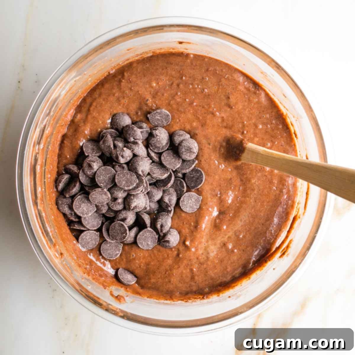Dark chocolate chips being folded into the tahini brownie batter in a large glass bowl, ensuring even distribution.