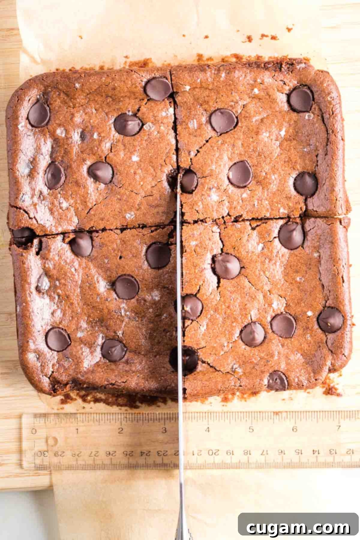 Brownies being cut into precise quarters with a sharp chef's knife and a ruler for accuracy.