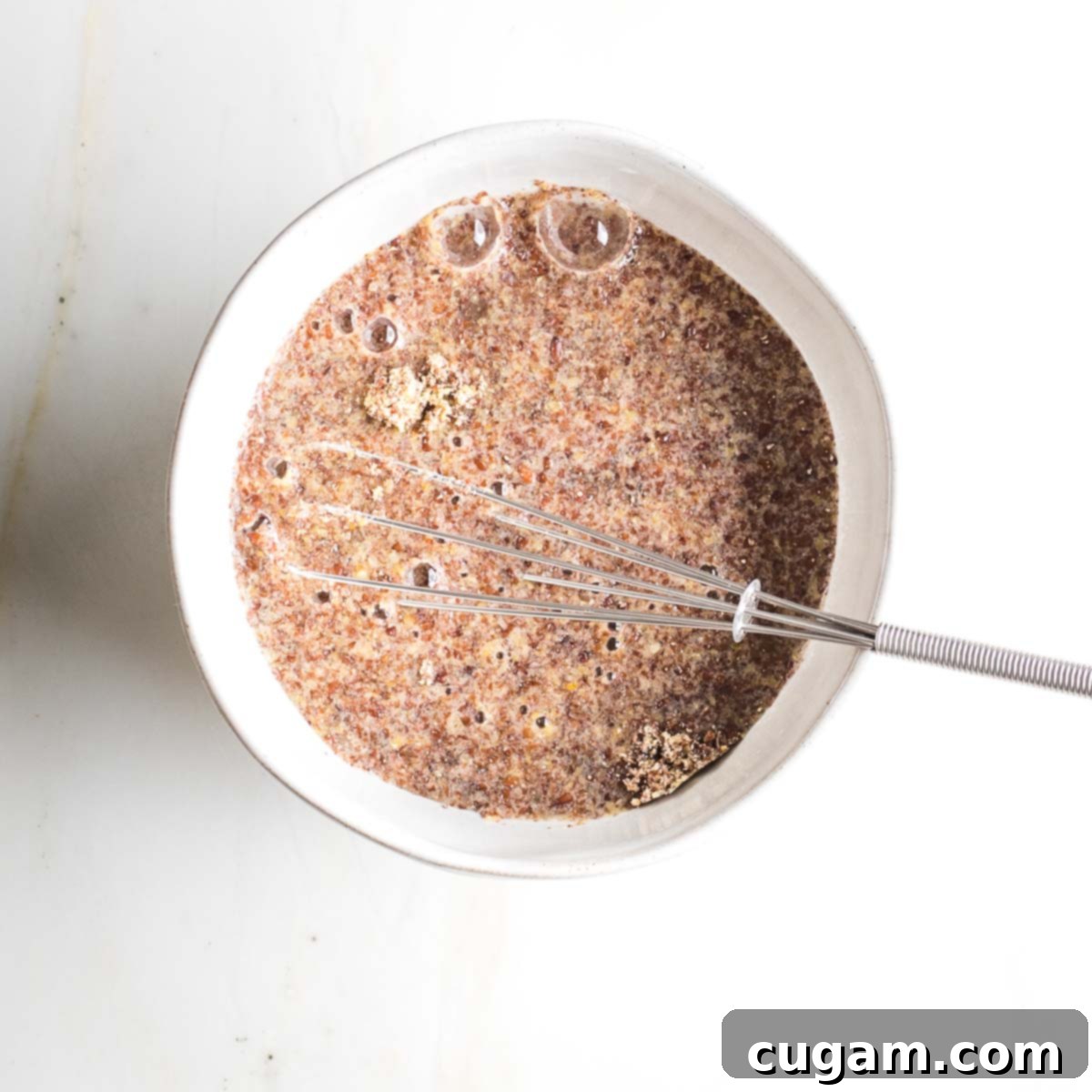 Flax eggs gelling in a bowl with a small whisk, showing the thickening process.