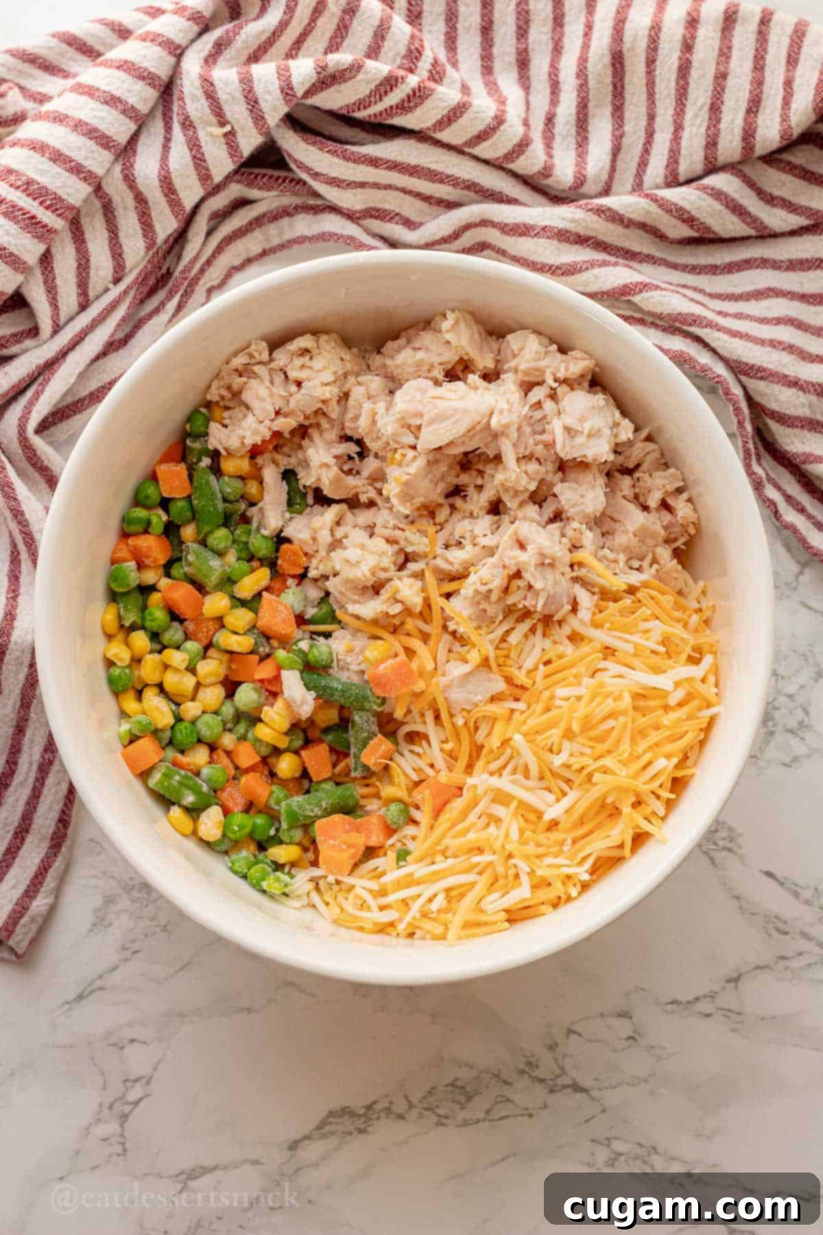 Chicken and Rice Vegetable Casserole 5 Cheese, chicken, and frozen veggies in white bowl.