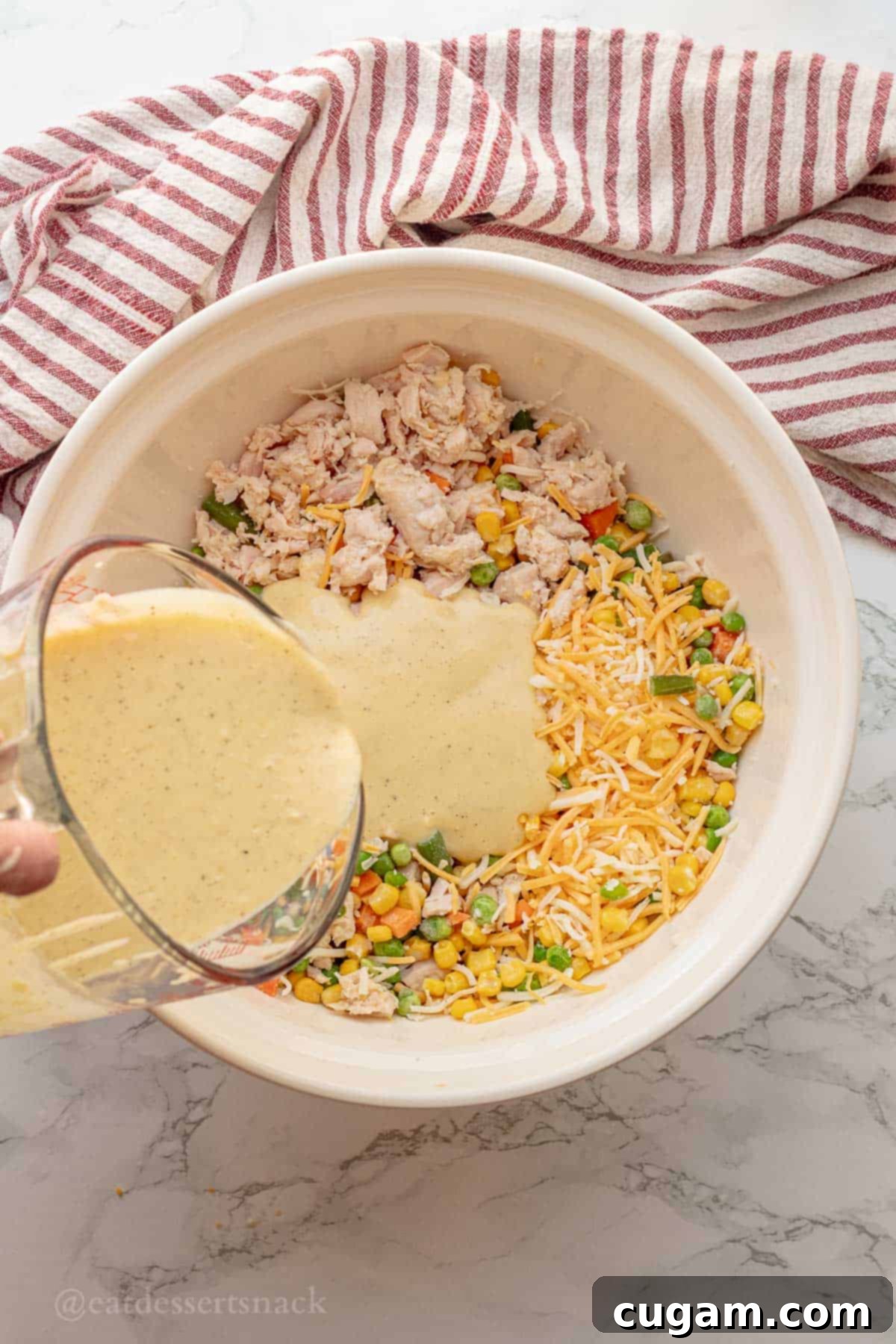 Chicken and Rice Vegetable Casserole 7 Pouring sauce into bowl of chicken, veggies, and cheese.