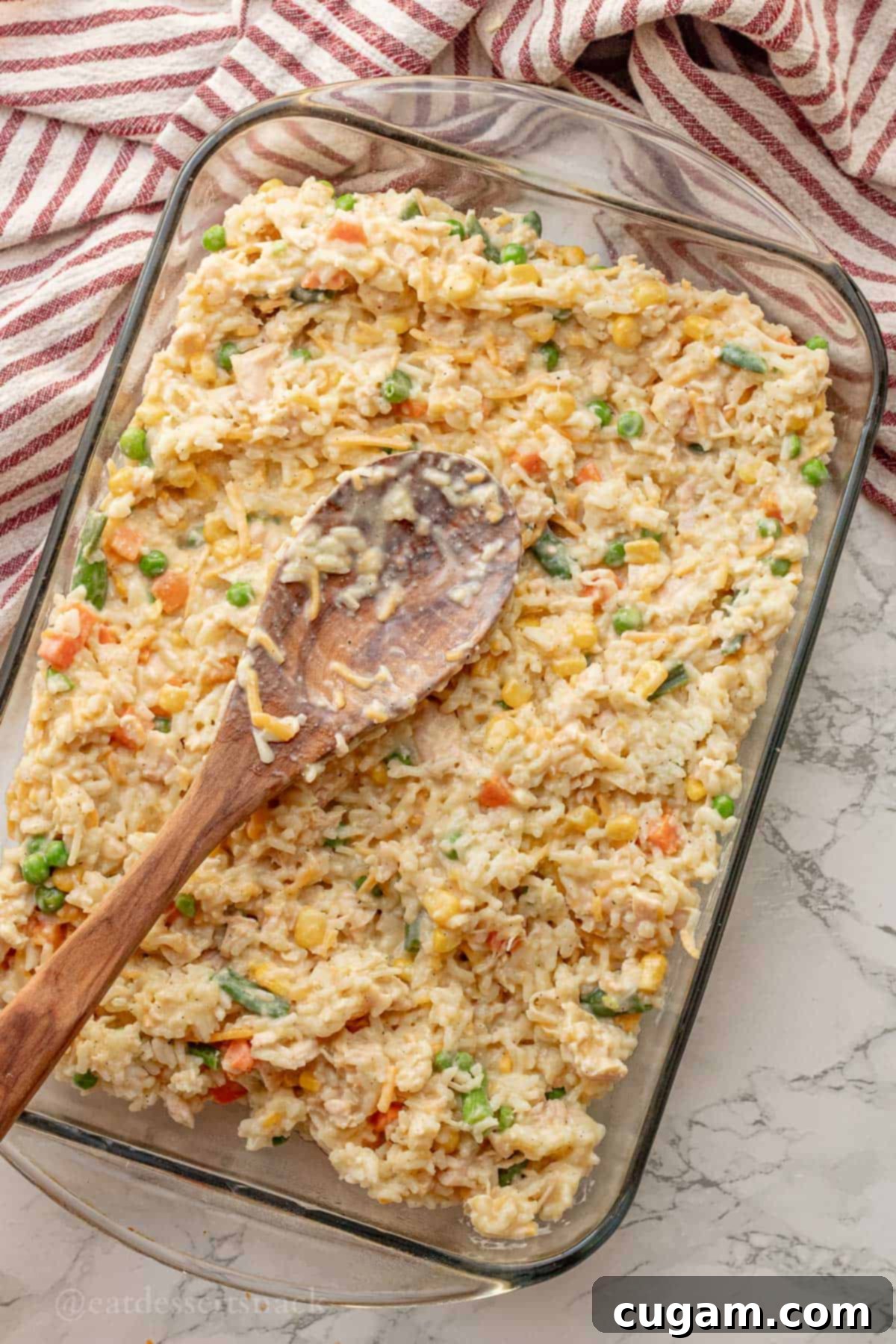 Chicken and Rice Vegetable Casserole 9 Spreading unbaked chicken and veggies and rice in glass pan with wooden spoon.