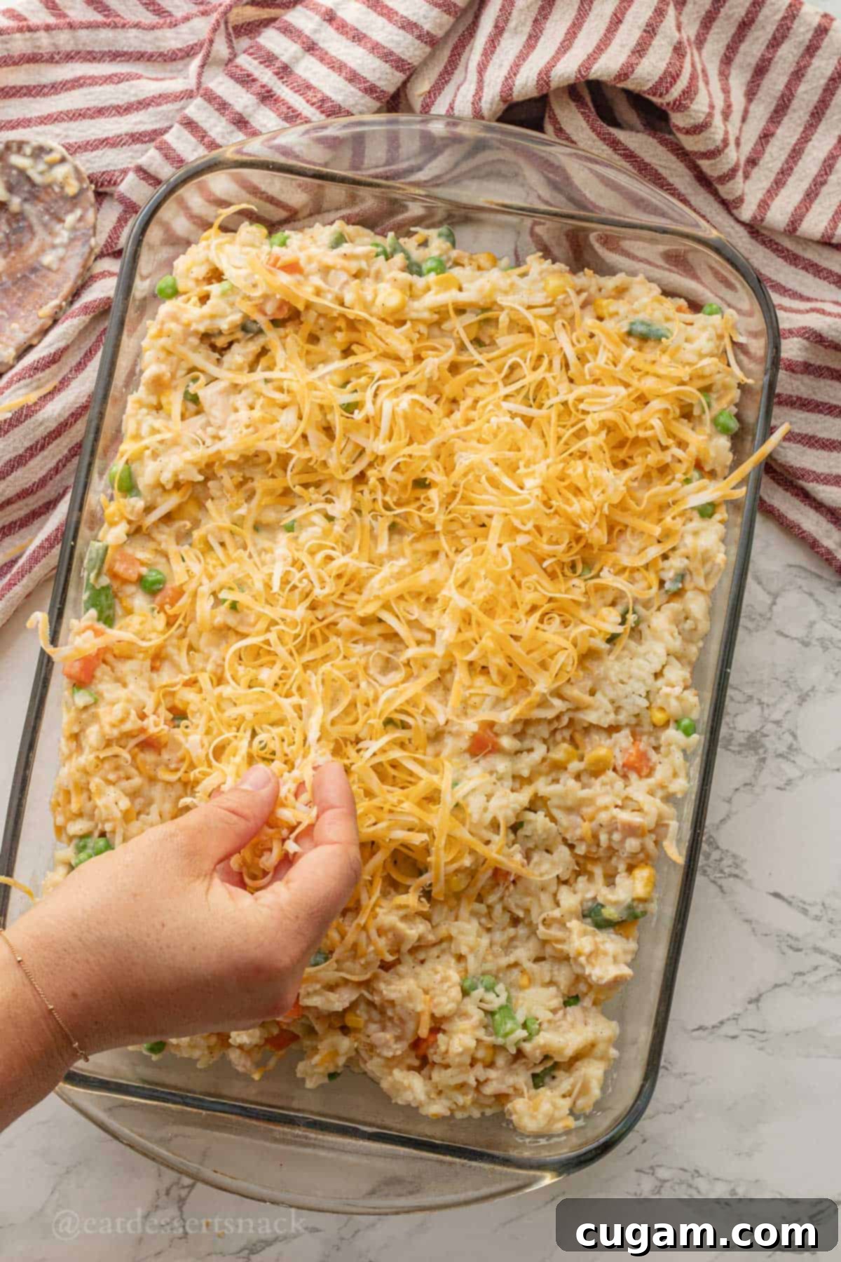 Chicken and Rice Vegetable Casserole 10 Sprinkling cheese over raw chicken and rice in glass pan.