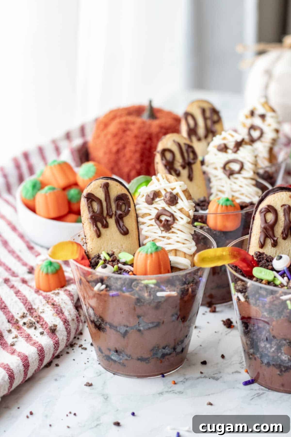 A completed Halloween dirt pudding cup, decorated with gummy worms, a headstone cookie, a mummy cookie, and pumpkin candy.