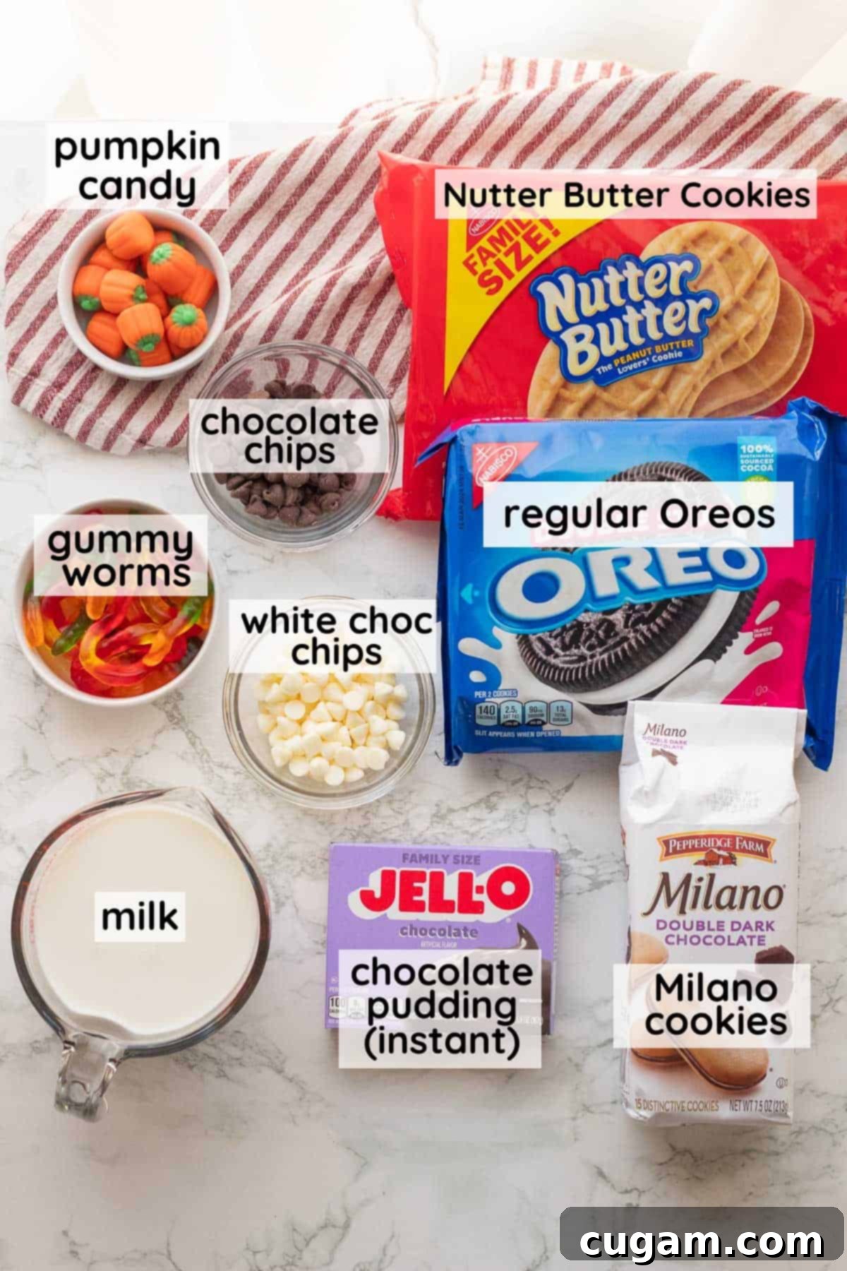 Labeled ingredients for Halloween Pudding Cups in glass bowls on a marble countertop, including instant pudding mix, Oreos, milk, and various candies.